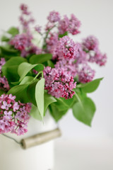 Bouquet of pink lilac in a white metal can on a light background. 