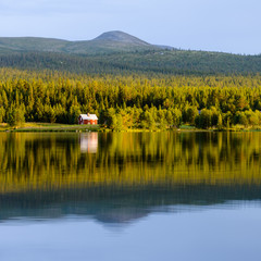 House and trees reflected on still lake, Sweden
