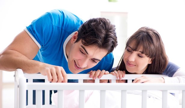 Happy Young Family At Baby Bed Cot