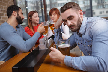 Young drunk man sleeping after drinking too much beer, his friends on background. Handsome man asleep at beer pub during meeting with friends