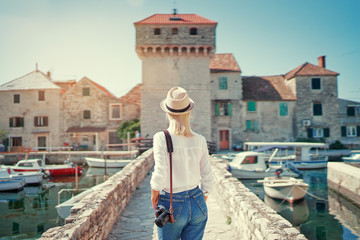 Fototapeta na wymiar Photography and travel. Young woman walking with her camera near Kastel Gomilica Castle on Dalmatia coast, Croatia.