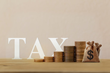 Finance tax concept: US dollar bags with rising coins, word tax on wood table. depicts ad valorem...