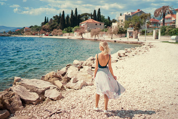 Tourism concept. Young traveling woman enjoying the view of Kastel Castle walking near the sea on Croatian coast.