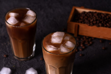 Iced coffee in a tall glass with cream poured over. Wood background. Low key.