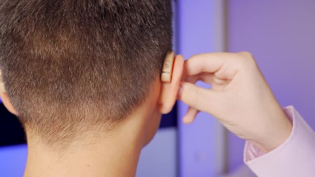 A young man takes off and puts on a digital hearing aid. Fourth degree hearing loss. Bilateral sensorineural hearing loss