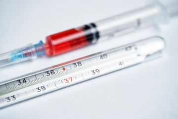 Thermometer on a white background Syringe with red medicine for lowering temperature.