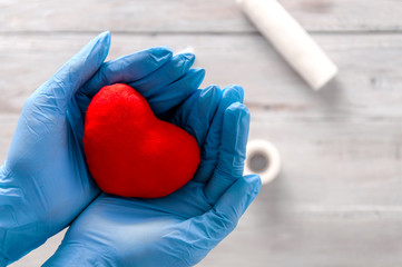 A girl in medical gloves holds a heart in her hands. Bandage, pills, syringe and heart on a gray wooden background. Health care. Ambulance. First Aid Kit. Healthcare and medicine.