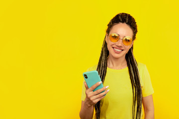 Happy smiling woman with bright phone in the yellow studio