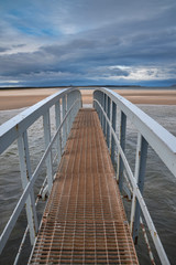 Fototapeta premium Publiczna kładka przy plaży Belhaven w Szkocji. Odetnij podczas przypływu. Koncepcja most donikąd, nieznane, podróż, przygoda.