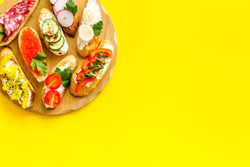 Set of bruschetta on cutting board on yellow background top-down copy space