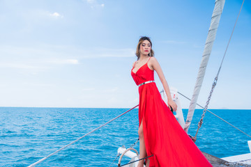 Beautiful young sexy woman in red dress and makeup, summer trip on a yacht with white sails on the sea or ocean in the Gulf marine of the wind and the breeze.