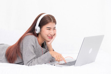 Beautiful woman long hair wearing gray sweater relaxing listening to music with headphones at bed with laptop on white curtain background. © Look Aod 27