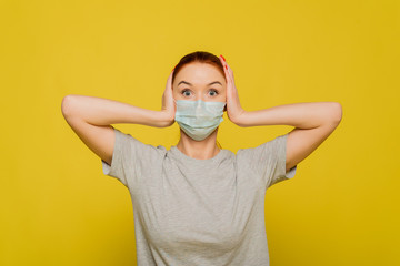 A beautiful woman clings to her head and is shocked by the spread of the coronavirus. Red-haired beautiful girl in a protective mask on a yellow background. The concept of protection and prevention