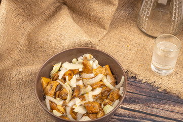 Salted mushrooms with onions in a ceramic bowl , a glass of vodka and a decanter on a background of rough homespun fabric. Close up.