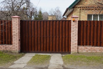 brown closed private gate and part of a fence of wooden boards and bricks on a rural street in...