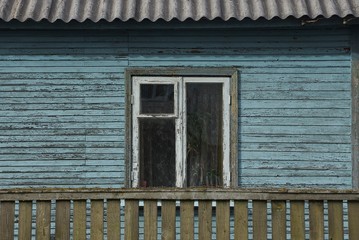 one white old window on a blue wooden wall of a rural house behind a green fence
