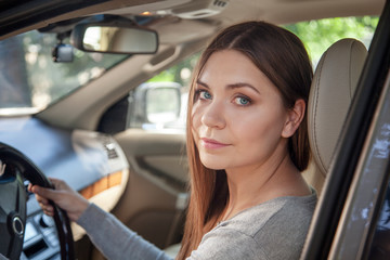 Fototapeta na wymiar Young attractive caucasian woman with blue eyes and dark hair behind the wheel, driving a car. Happy smile, positive emotions, pretty sunny day. Outdoors, copy space.