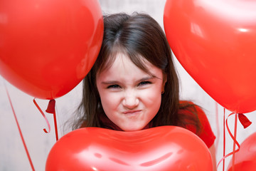 little naughty angry girl face close up among red heart-shaped balloons