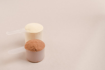 Whey protein powder in scoop and plastic shaker on neutral beige background