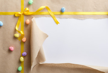 Top view of decorative easter eggs on the craft wrapping paper, bright yellow bow and ribbon.Torn paper and empty space for congretulations