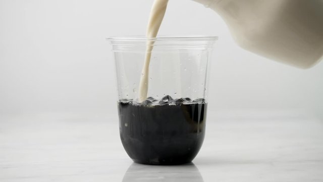 Pouring milk tea in Plastic glass with tasty popular tapioca pearl bubble on white table. 4K video shot.