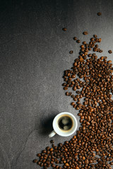 Vertical top view of coffee beans and cup, on a dark ardesia table