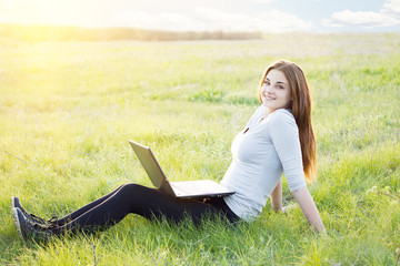 girl working in nature with a laptop lying on the green grass.