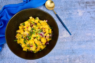 Fresh homemade mango salsa in a bowl on blue background
