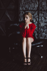 Fototapeta na wymiar Beautiful woman lady in a red dress sits sadly on a leather chair in a loft style. Soft selective focus. Beauty, fashion.