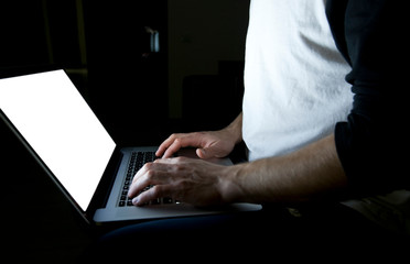 The young man sitting on the sofa  with modern laptop in the evening and surfing the web