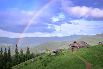 Beautiful mountains landscape with rainbow, green meadow and wooden house. Carpathians, Ukraine.