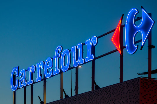 The illuminated neon sign of the French supermarket chain Carrefour at sunset