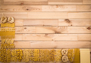 Different kind of raw pasta on a wooden table - mediterranean food concept, large choice of types and shapes