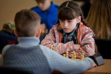 A girl plays chess. Game of chess. Tournament. A girl plays against a boy.
