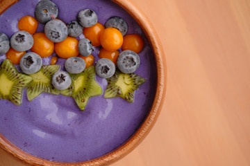 Smoothies of violet color from banana and currant, on top of a blackberry, physalis and kiwi berry. Smoothies in a wooden bowl.
