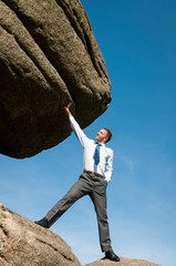 Strong businessman holding a massive boulder with a single hand in blue sky copy space