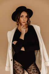 Beautiful girl in a black bodysuit and a black hat and a white jacket on a gold background