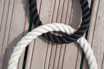 Thick loops of black and white nautical rope embracing outdoors on a wooden background