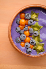 Smoothies of violet color from banana and currant, on top of a blackberry, physalis and kiwi berry. Smoothies in a wooden bowl.