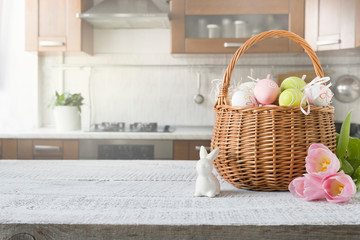 Wicker basket with bunny, tulip, easter colorful eggs on kitchen wooden table. Spring easter composition. Space for text.