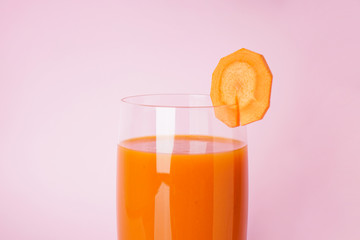 Fresh carrot juice in a glass cup on a pink background, close-up
