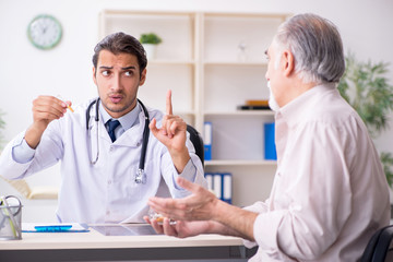Young male doctor and old patient in antismoking concept
