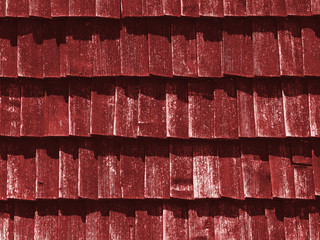 Red texture of wooden tile roof. Shingle aged wooden Background. Backdrop with small overlapping colored wooden shingles on roof