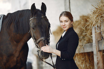 Obraz premium Woman standing near horse. Rider in a black uniform. Girl feeds horse hay