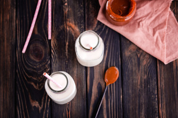 Two bottles of fresh milk with tubes and fresh homemade salted caramel n dark background.
