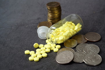 A bottle of pills and coins on a gray background. The concept of drug costs, treatment