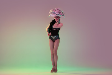 Spring mood. Young female dancer with huge floral hats in neon light on gradient background. Graceful model, woman dancing, posing. Concept of carnival, beauty, motion, blooming, spring fashion.