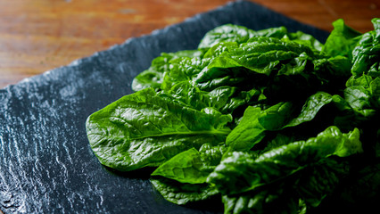 Healthy vegan food concept: close-up backlight of freshly picked green spinach leaves placed on a slate plate and wooden table with bokeh effect
