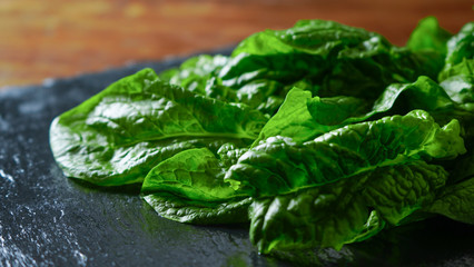 Healthy vegan food concept: close-up backlight of freshly picked green spinach leaves placed on a slate plate and wooden table with bokeh effect