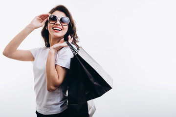 Happy cute female customer with black paper bags adjusting sunglasses isolated white background copyspace